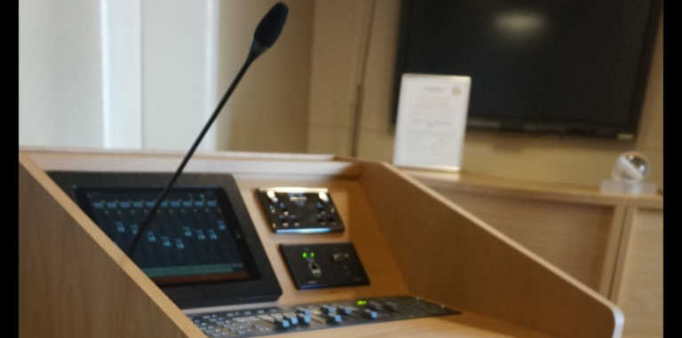 AV lectern Wooden podium with a microphone and control panel, set in a conference room.